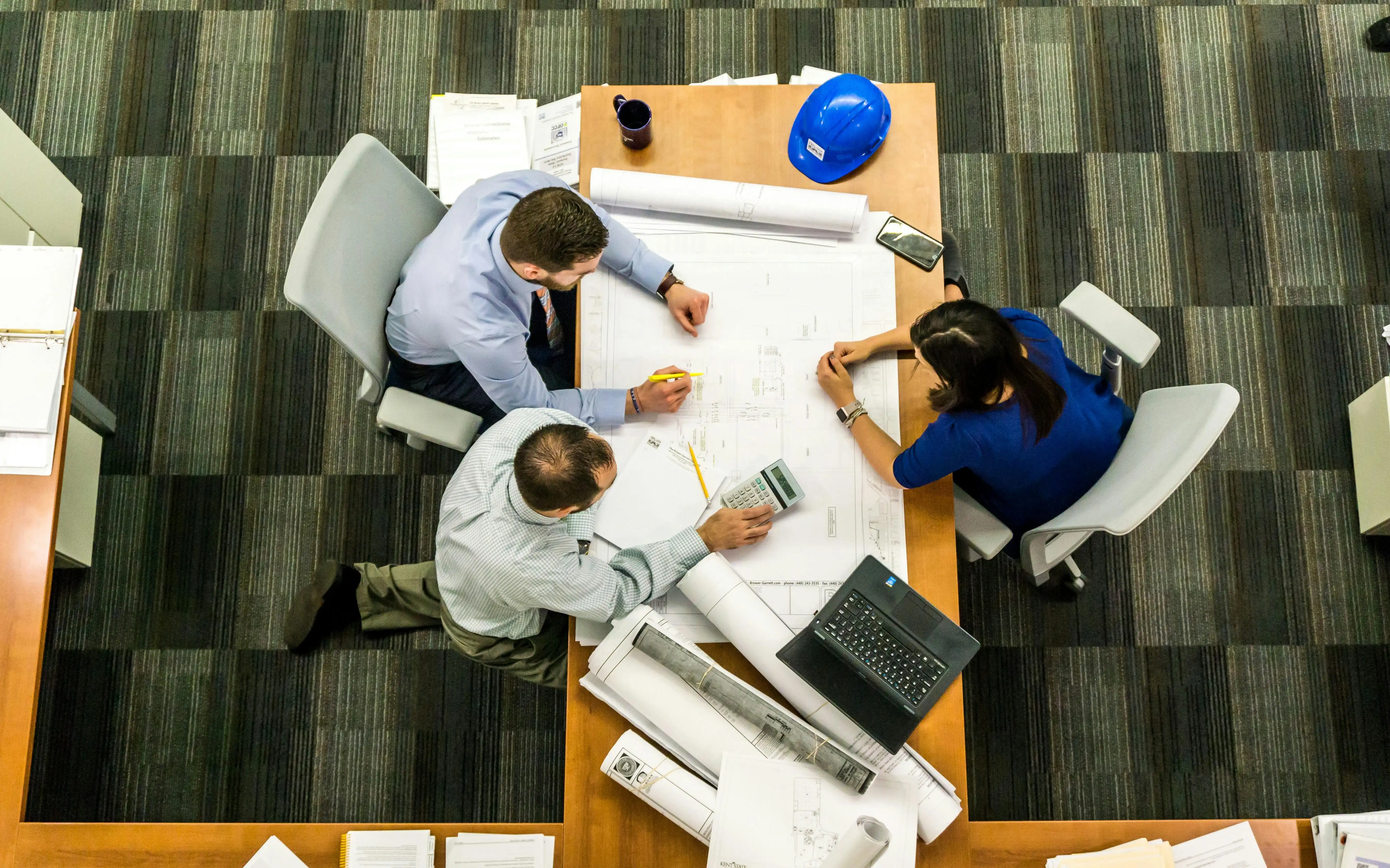 A group of architects sitting around a table with draft plan sets and a computer.